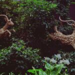 Duas Esculturas De Veados Estao Saltando Atraves Da Folhagem 774LwH4 kRE